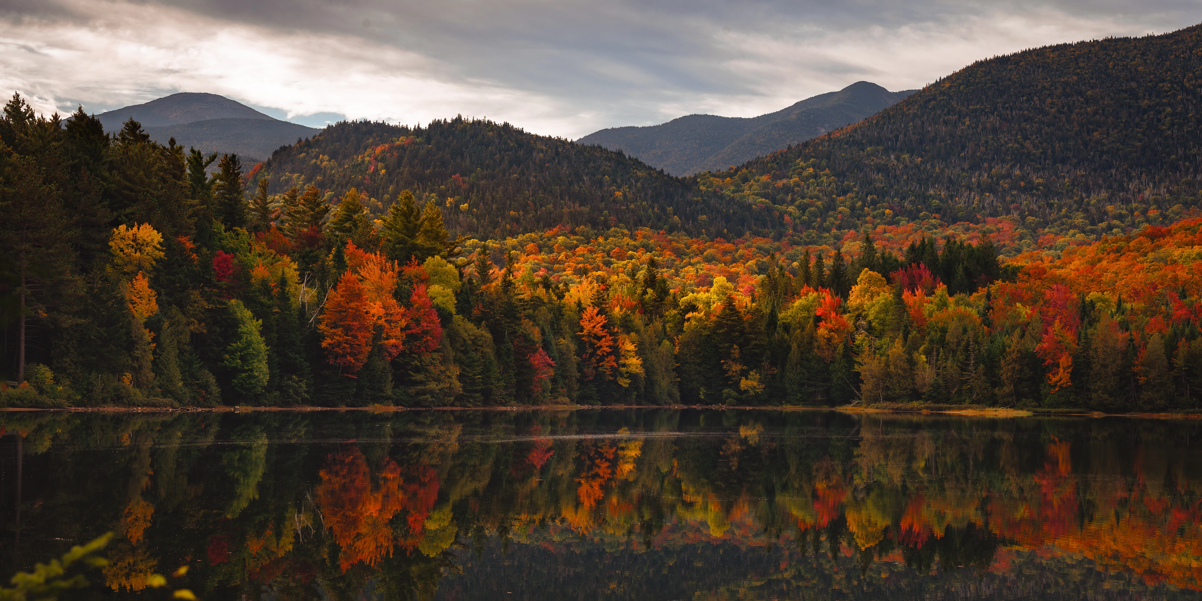 Autumn trees and the mountain skyline gather in the quiet surface of Heart Lake. Heart Lake, Adirondack High Peaks, New York.