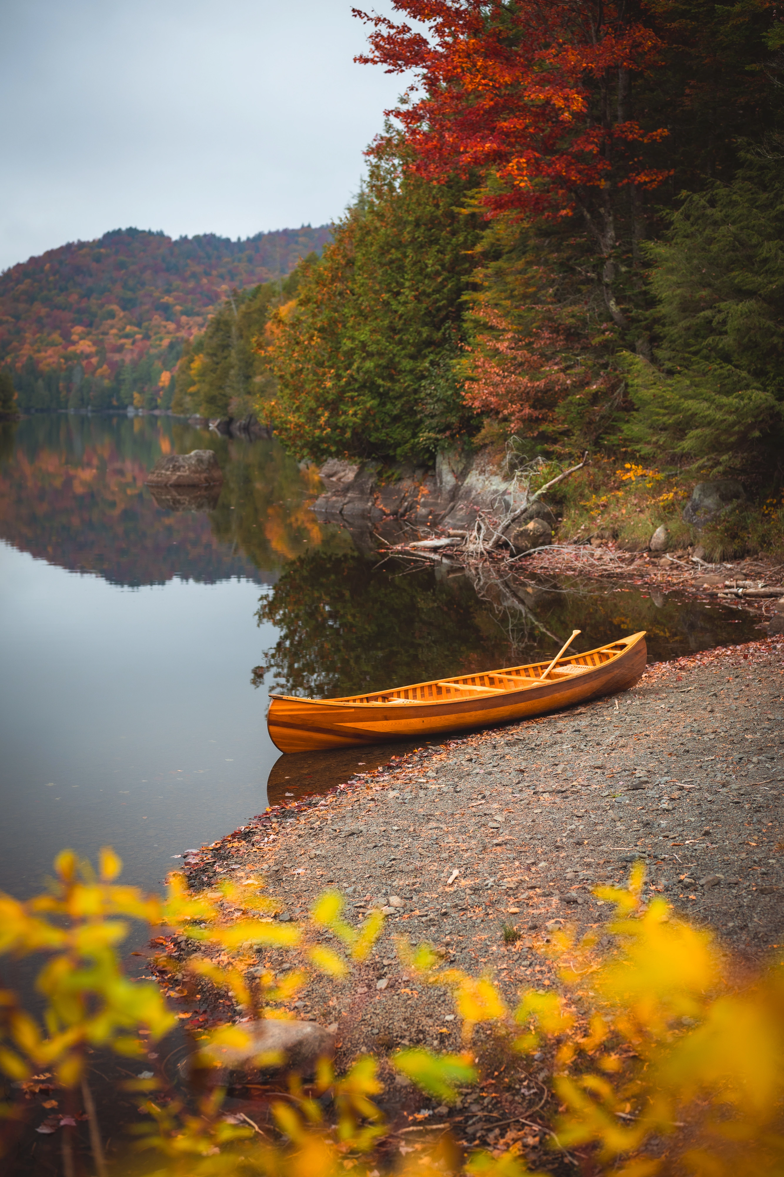 A handmade wooden canoe rests at Henderson Lake's put-in, framed by yellow leaves and calm water. Henderson Lake, Adirondack High Peaks, New York.