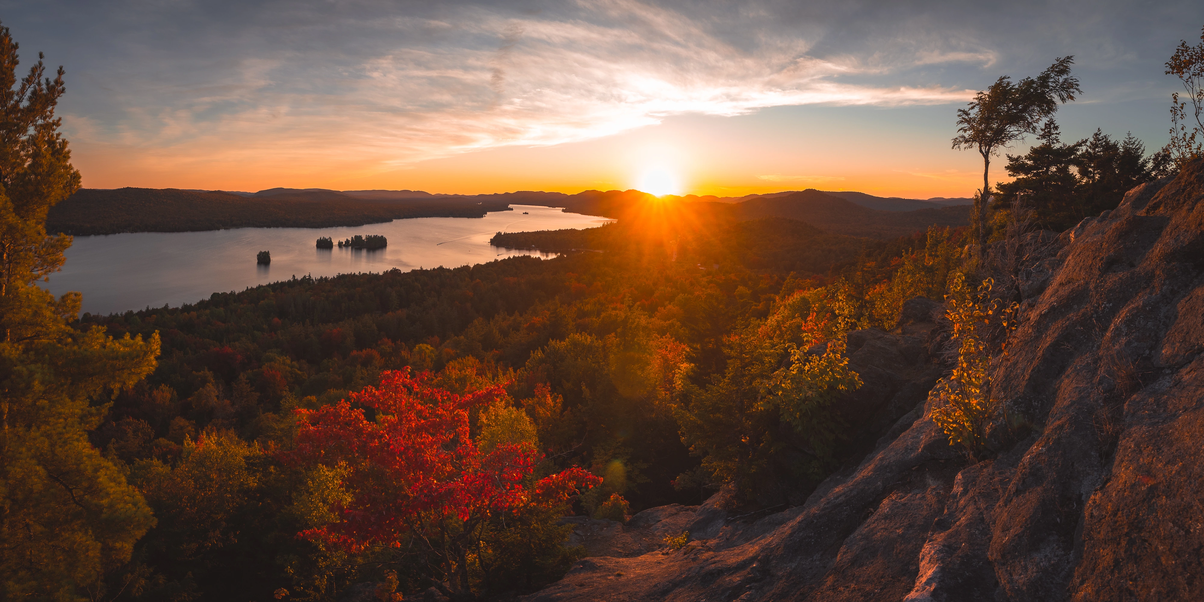 From Rocky Mountain near Inlet, New York, the setting sun rests over Fourth Lake while red leaves gather along the summit edge.